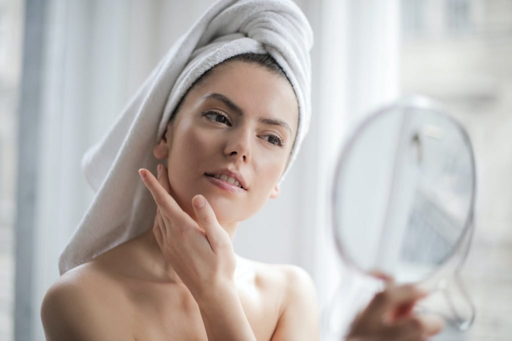 selective focus portrait photo of woman with a towel on head looking in the mirror