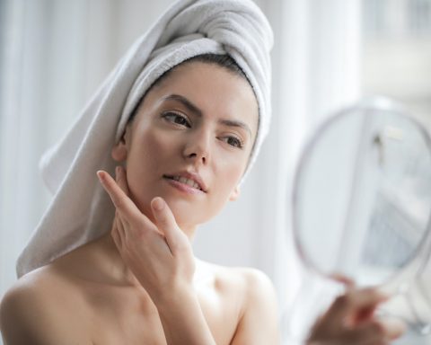 selective focus portrait photo of woman with a towel on head looking in the mirror